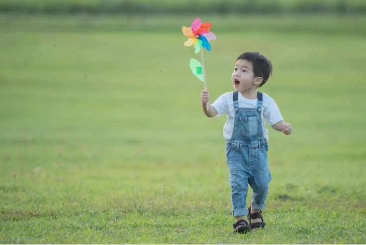 Cậu bé hoạt hình vui đùa với chiếc chong chóng màu sắc dưới ánh nắng